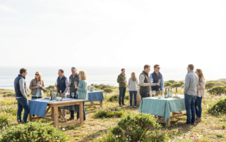 people enjoying an april wine tasting at tables by the ocean, with bottles and glasses.